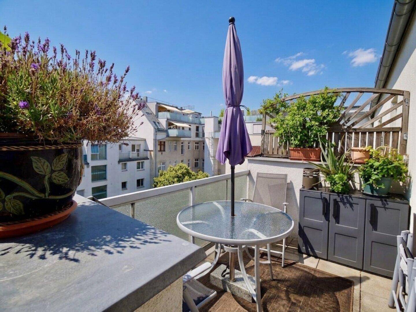 Balkon mit Sitzgelegenheiten, Sonnenschirm und Blick auf die umliegenden Gebäude.