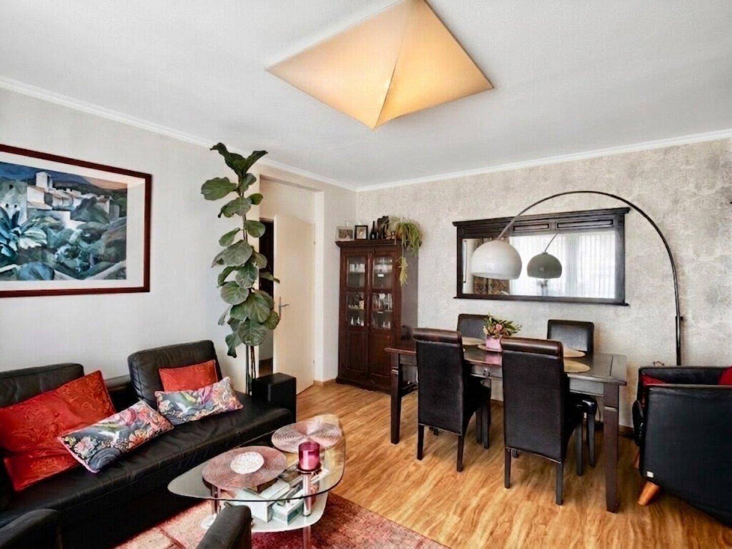 Gemütlicher Wohn-Essbereich mit dunklem Sofa, Esstisch und Holzboden.