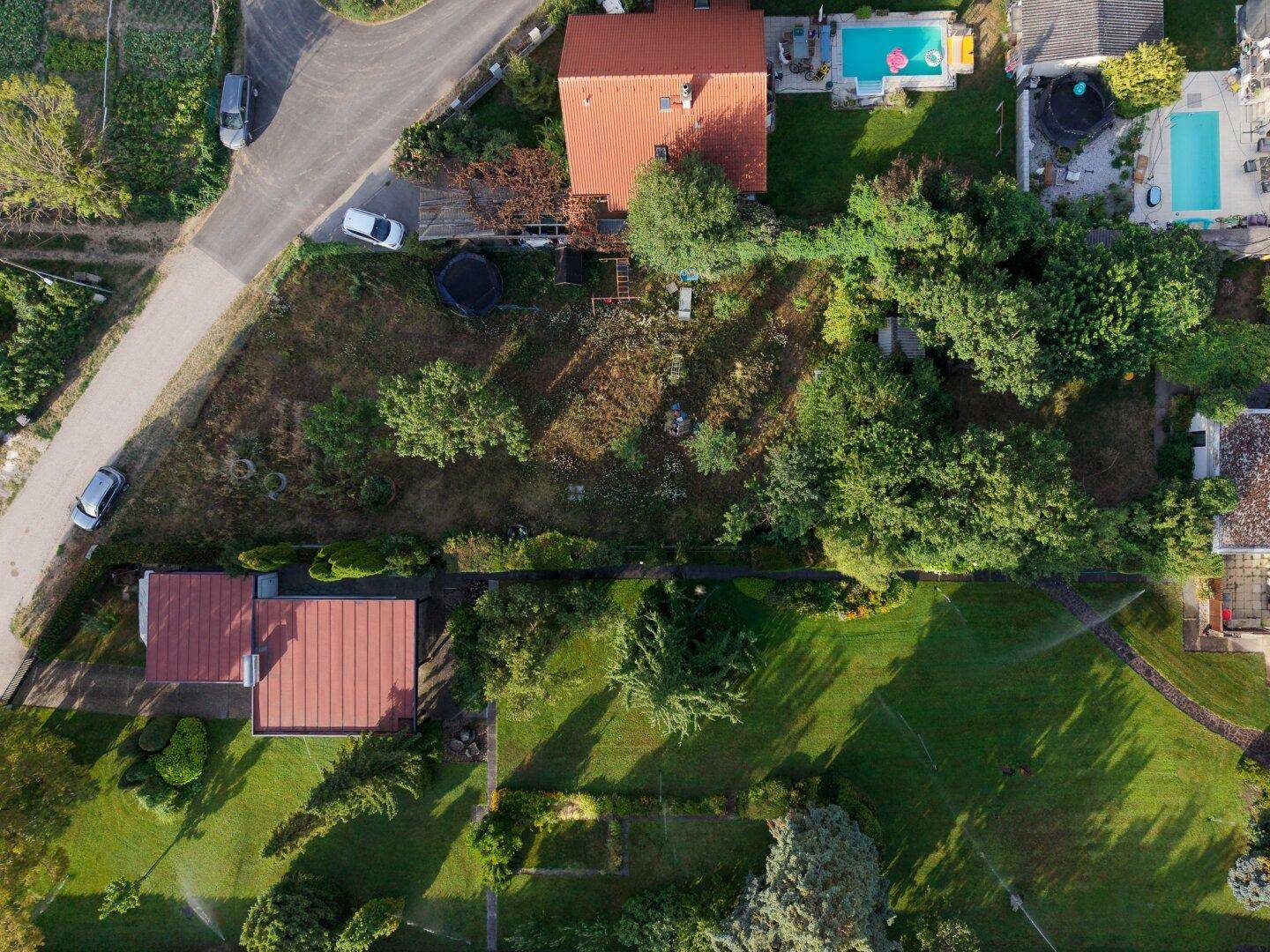 Draufsicht auf ein Grundstück mit Haus, Garten und angrenzenden Nachbargärten mit Swimmingpools.