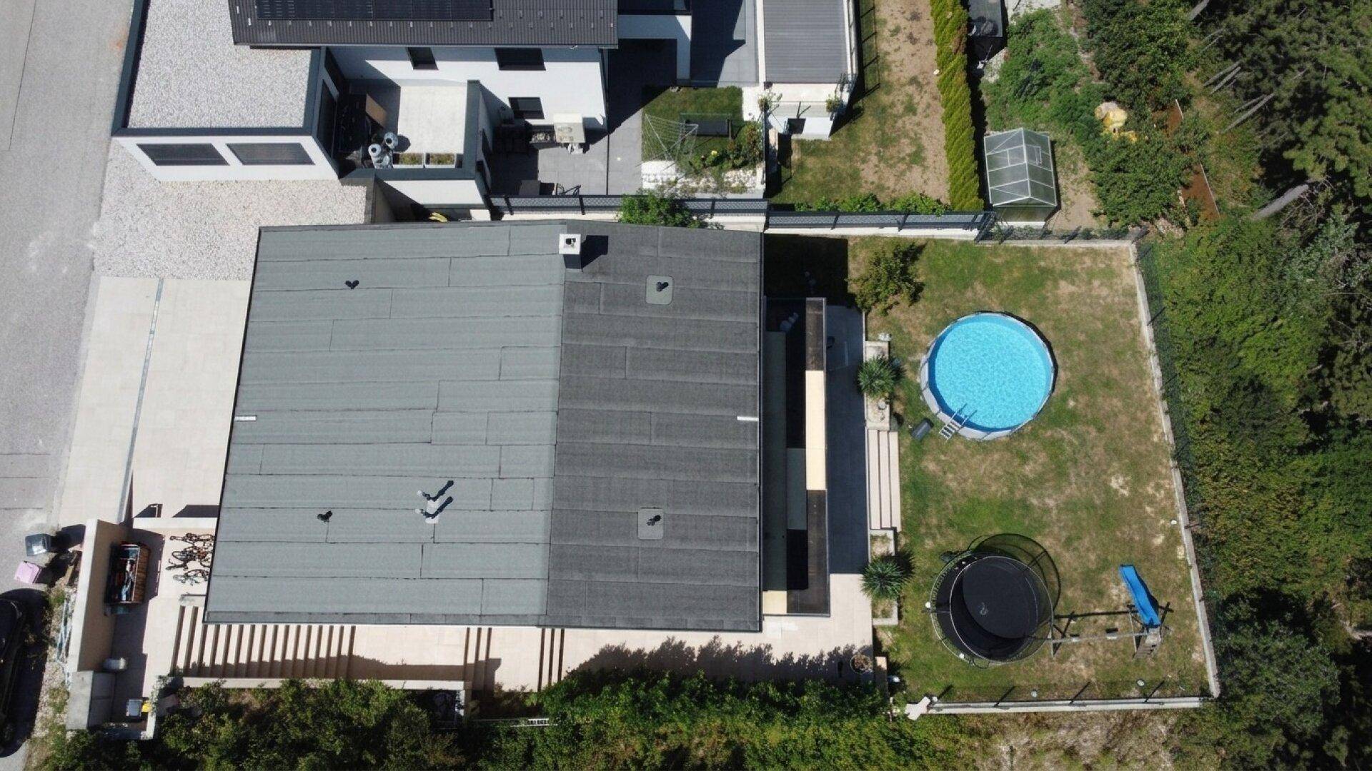 Draufsicht auf das Haus mit Flachdach, Garten, Swimmingpool und Trampolin.