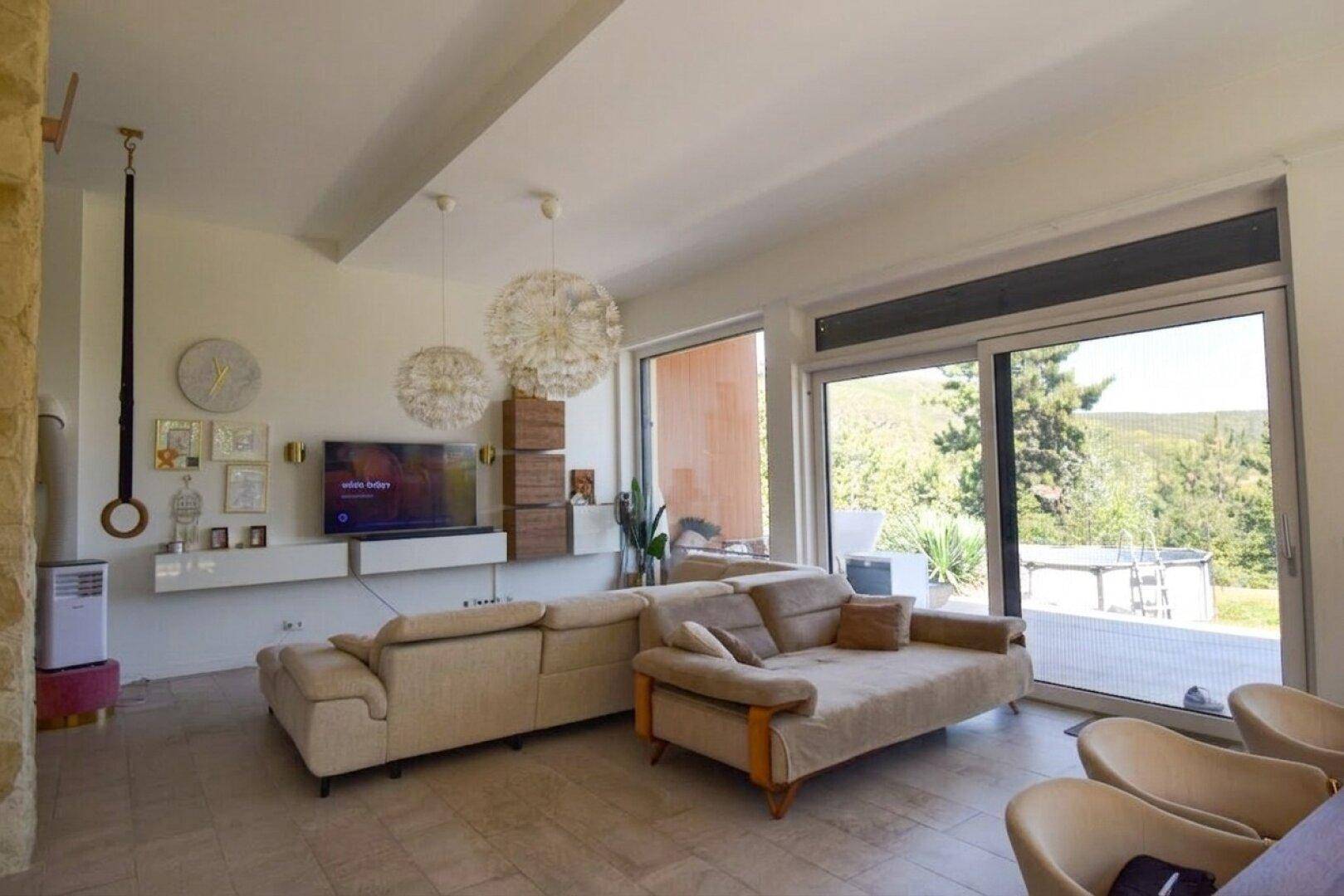Helles Wohnzimmer mit beigen Sofas, modernen Pendelleuchten und großen Schiebetüren zur Terrasse.