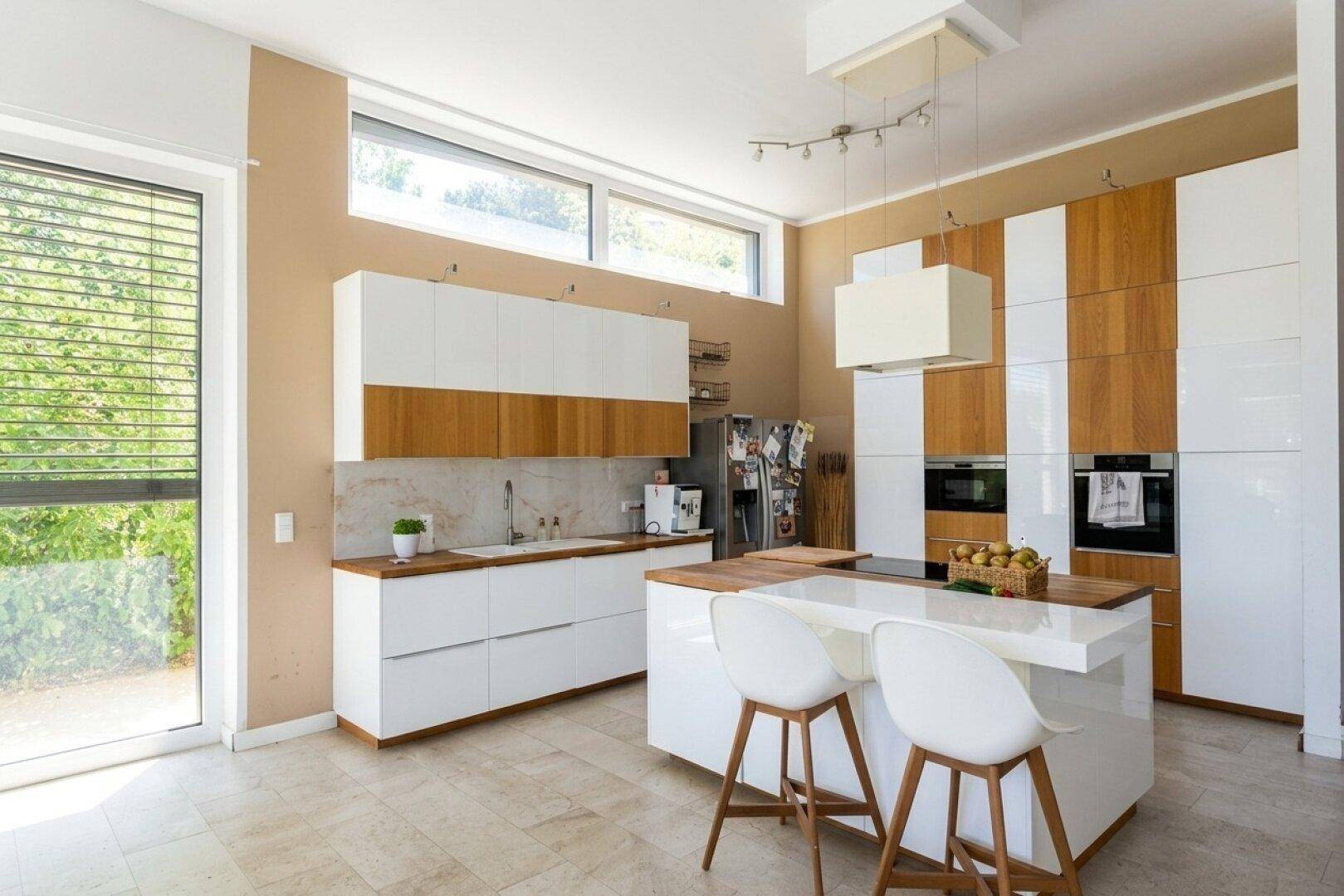 Moderne Küche mit weißen und holzfarbenen Schränken, Kücheninsel und Zugang zum Außenbereich.