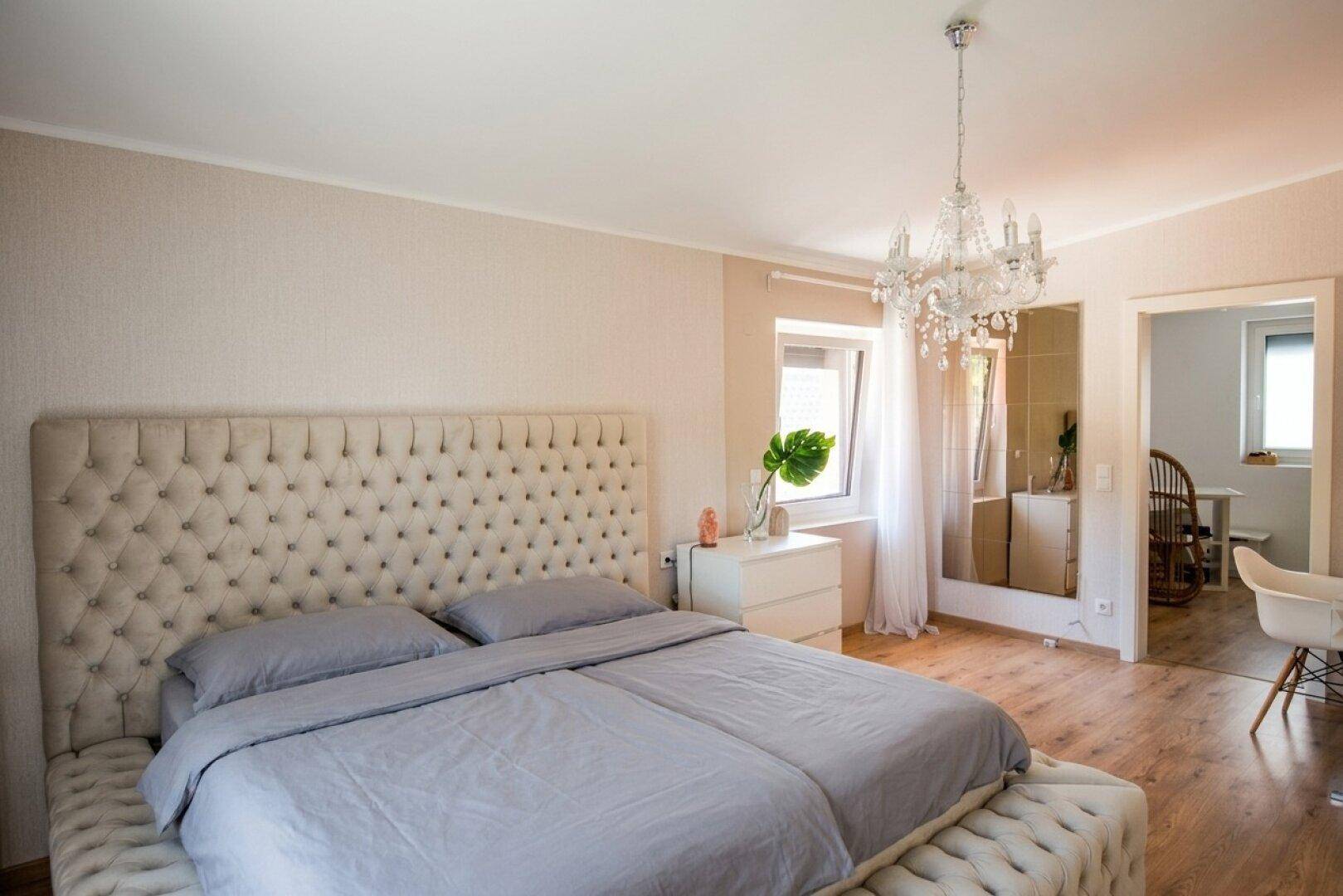 Gemütliches Schlafzimmer mit großem Polsterbett, Kronleuchter und Holzboden.
