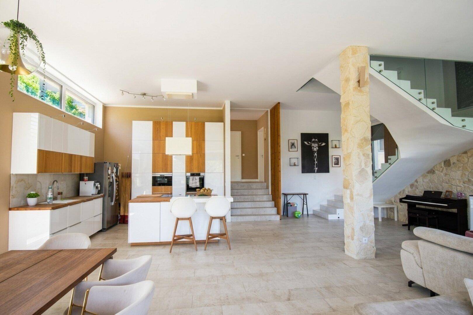 Offener Wohnbereich mit moderner Küche, Essbereich und eleganter Treppe mit Glasgeländer.
