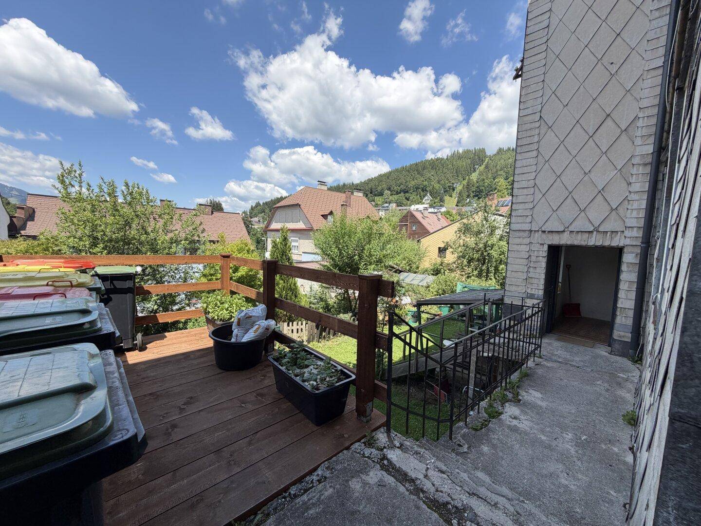Hölzerne Terrasse mit Mülltonnen und Blick auf die umliegende Bebauung und Hügel.