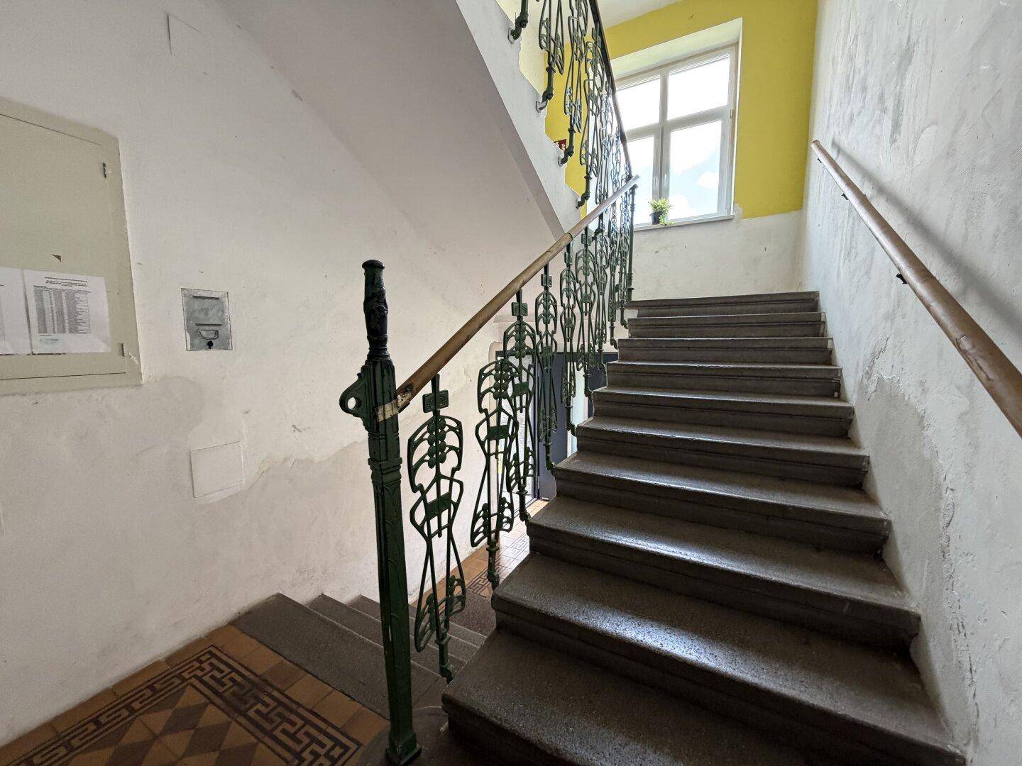 Historisches Treppenhaus mit Steinstufen, kunstvollem Geländer und gelb gestrichenen Wänden.