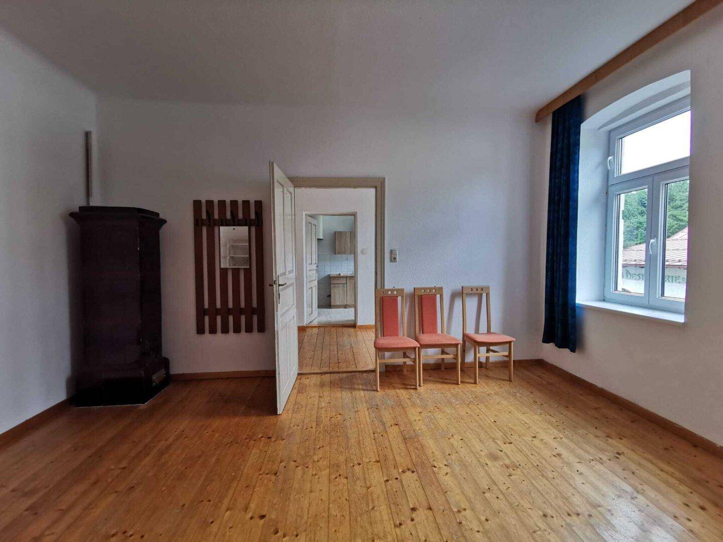 Geräumiges Wohnzimmer mit Holzdielenboden, weiß gestrichenen Wänden und traditionellem Kachelofen.