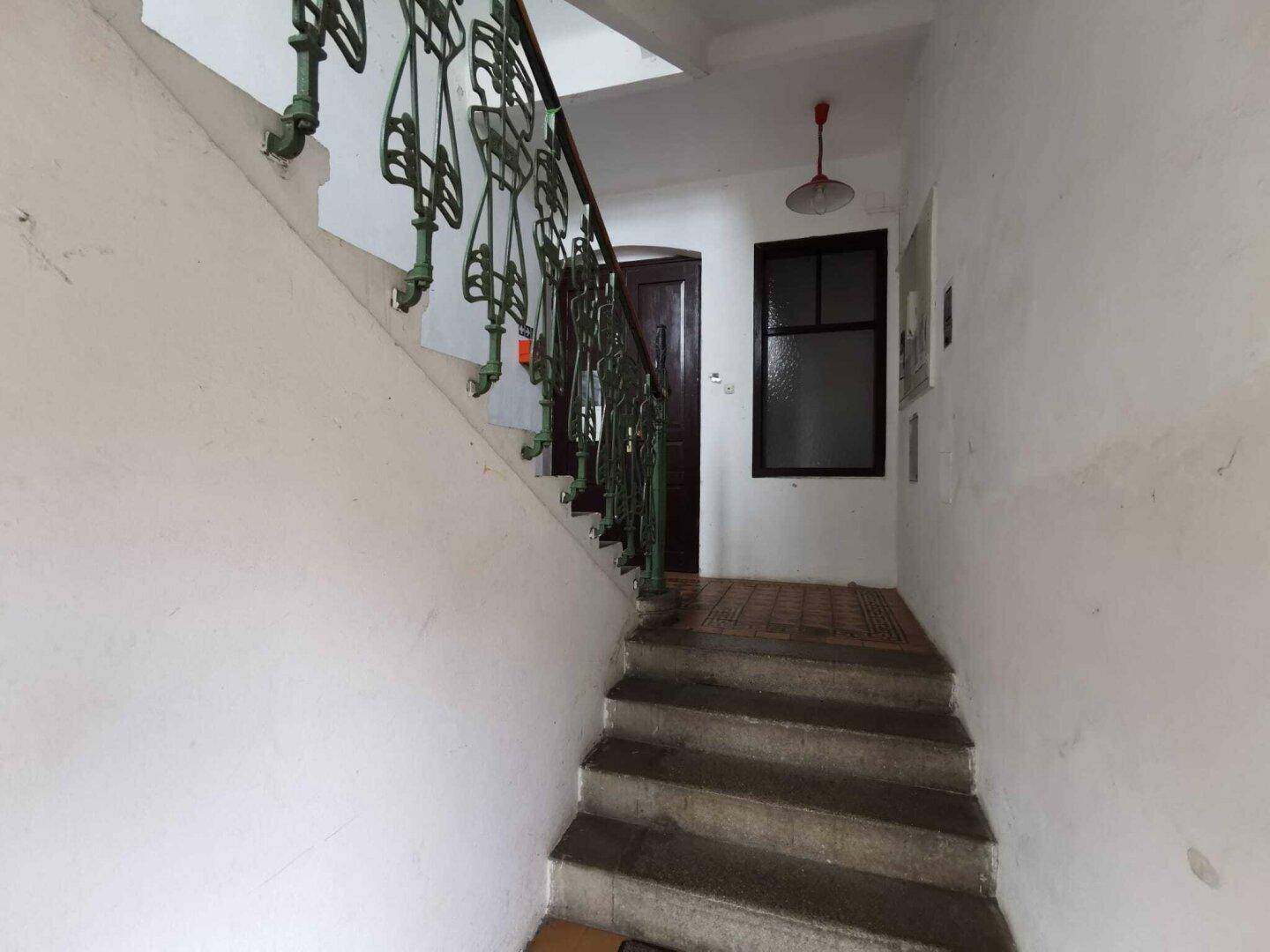 Treppenhaus mit Steinstufen und einem kunstvoll geschmiedeten Geländer in einem Altbau.