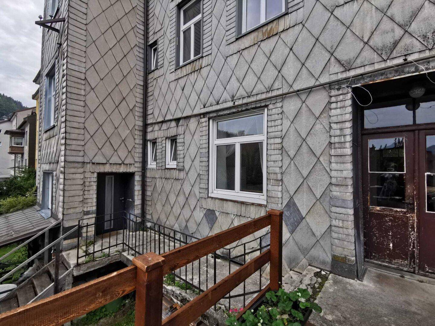 Fassade eines älteren Gebäudes mit Schieferverkleidung und abgenutzter Eingangstür.