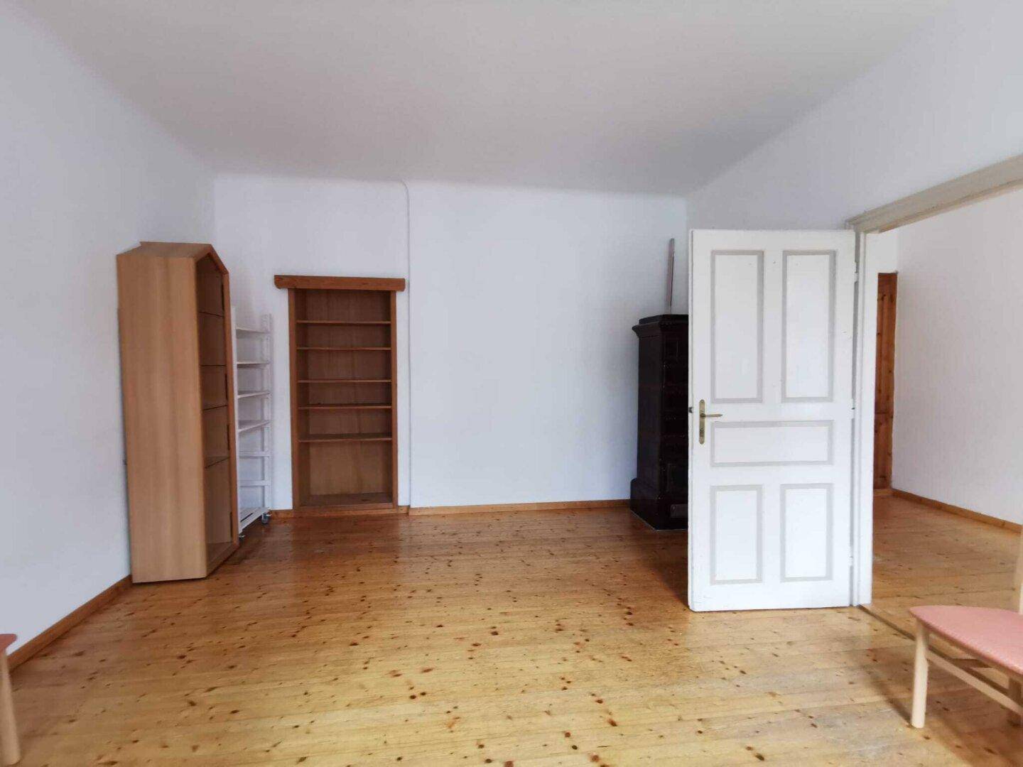 Heller Raum mit Holzdielenboden, weißen Wänden, eingebauten Regalen und einem Ofen.