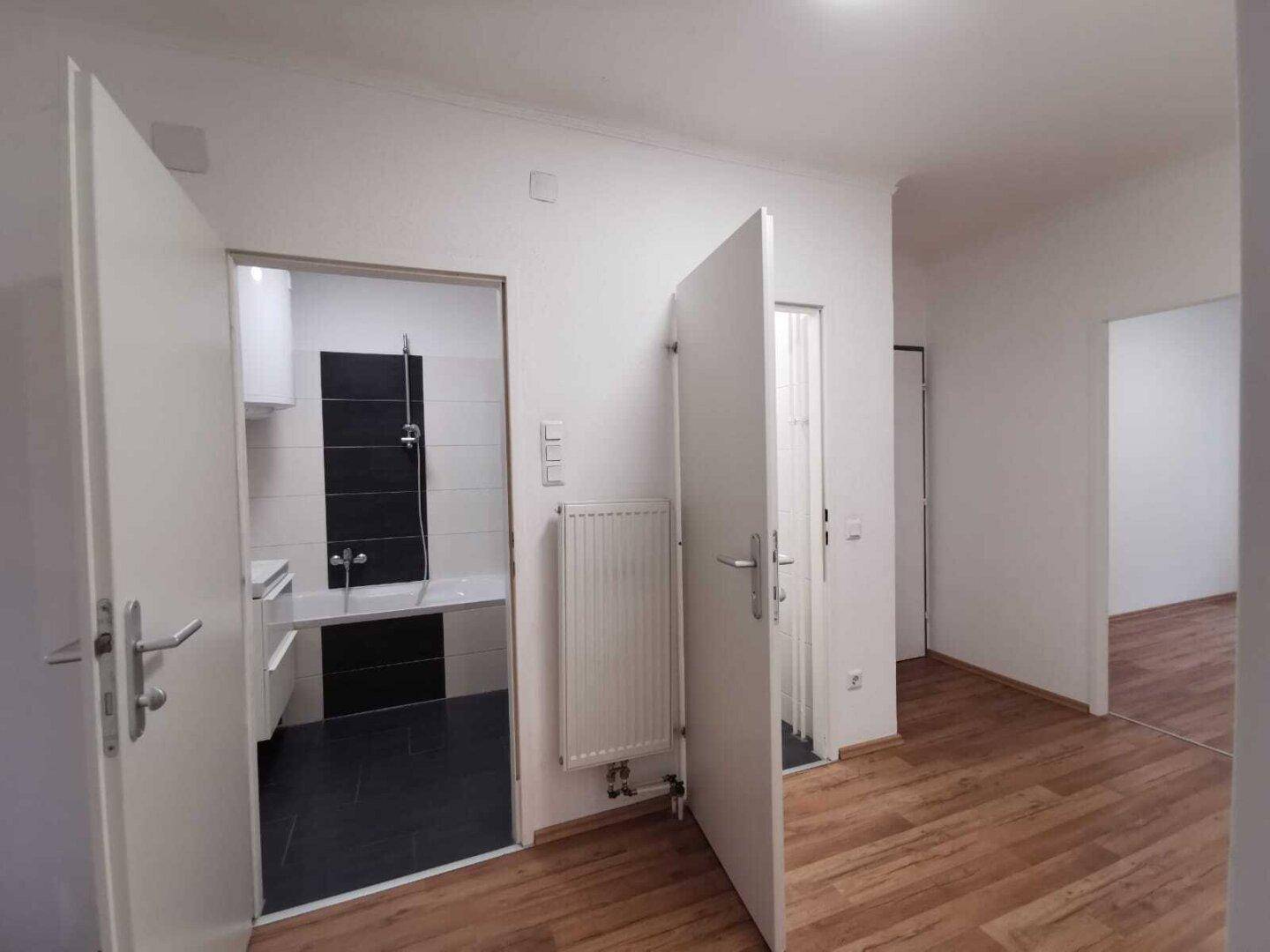 Heller Flur mit Laminatboden und Zugang zu einem modern gefliesten Badezimmer.