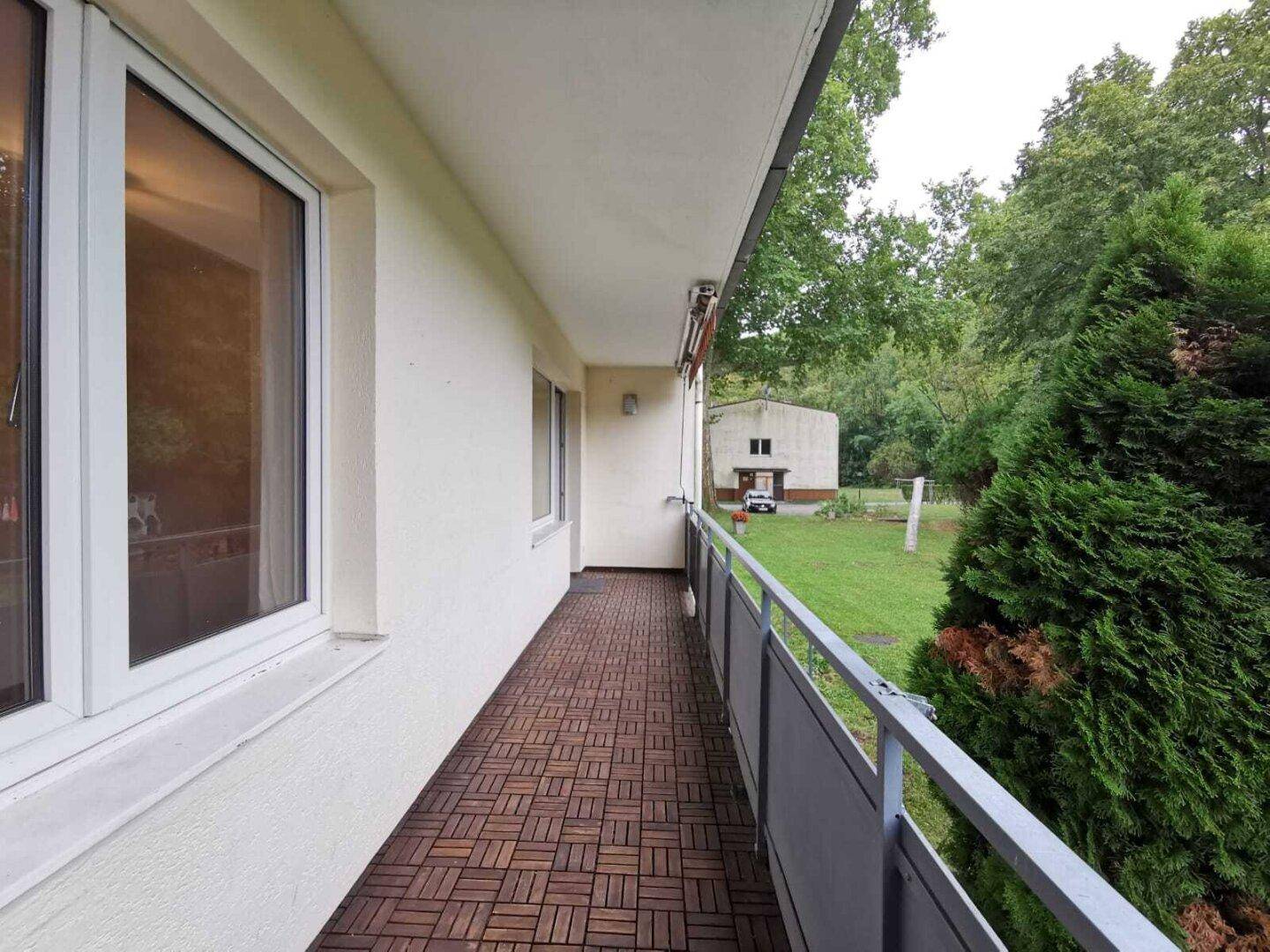 Geräumiger Balkon mit Holzdielen und Blick auf eine weitläufige Grünfläche.