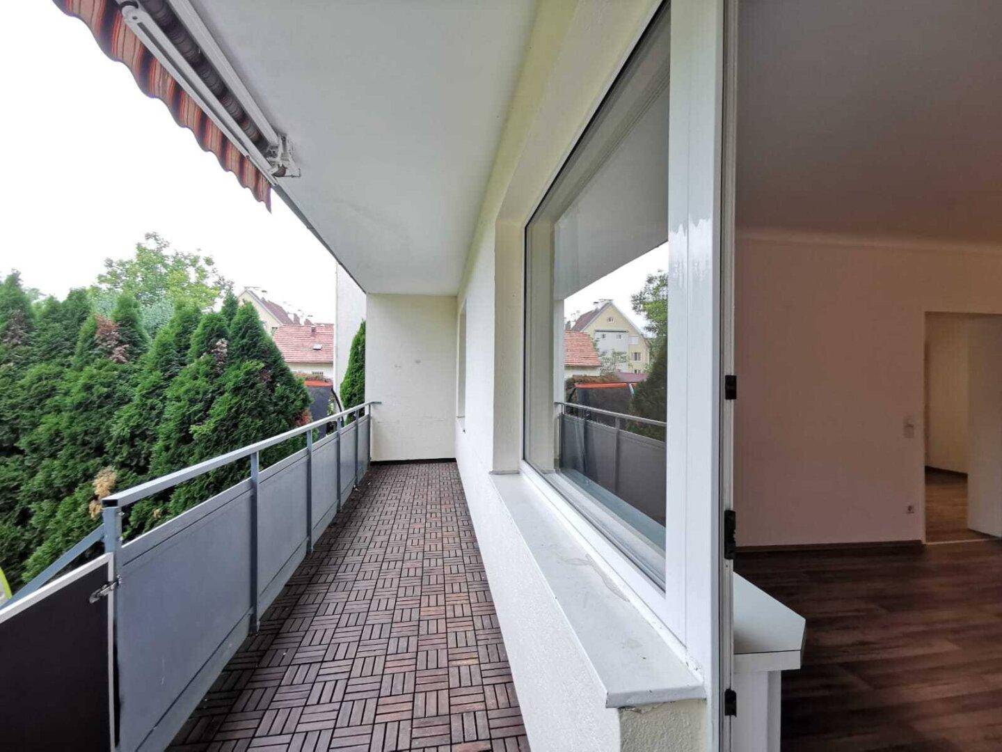 Langer Balkon mit Holzdielenboden und Markise, bietet Blick ins Grüne.