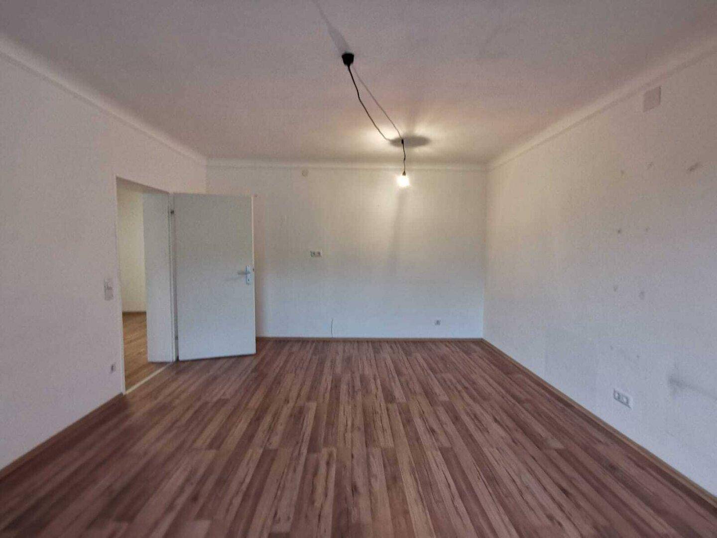 Leeres Wohnzimmer mit Laminatboden und weißen Wänden, bereit zur individuellen Gestaltung.
