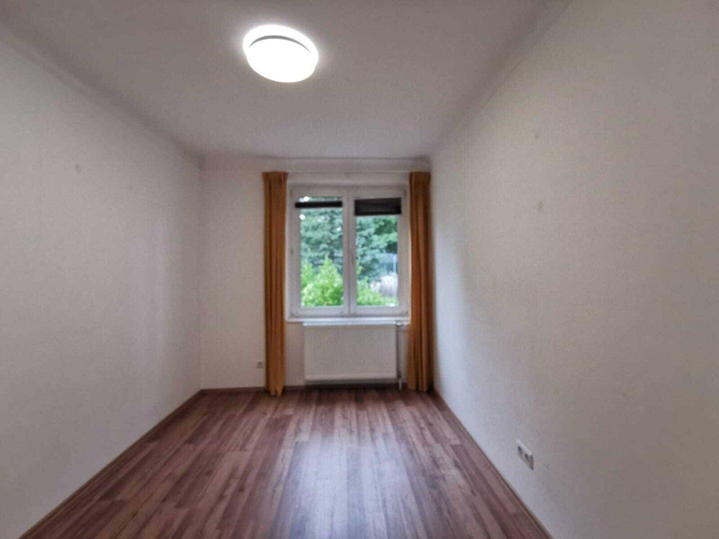 Ruhiges Zimmer mit Laminatboden und Fenster mit Blick ins Grüne.