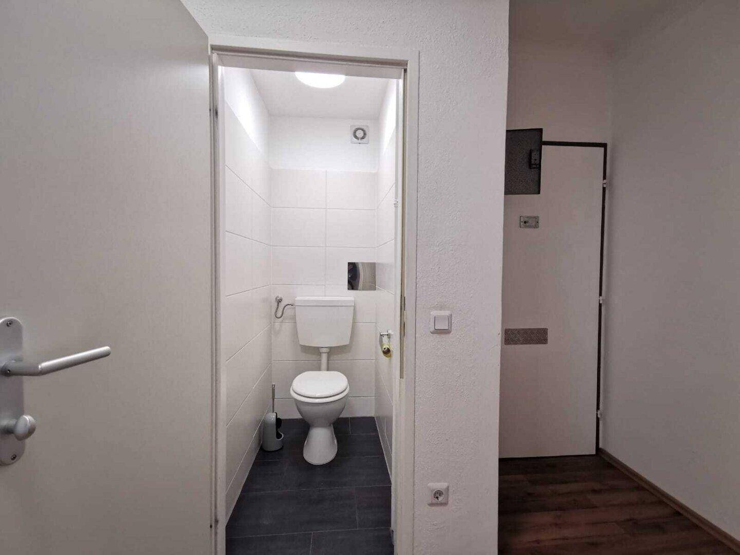 Modern gefliestes Gäste-WC mit wandhängender Toilette und Lüftung.