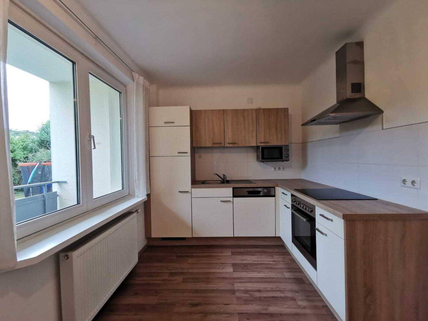 Funktionale Küche mit Einbauschränken, Herd und Mikrowelle, mit Blick nach draußen.