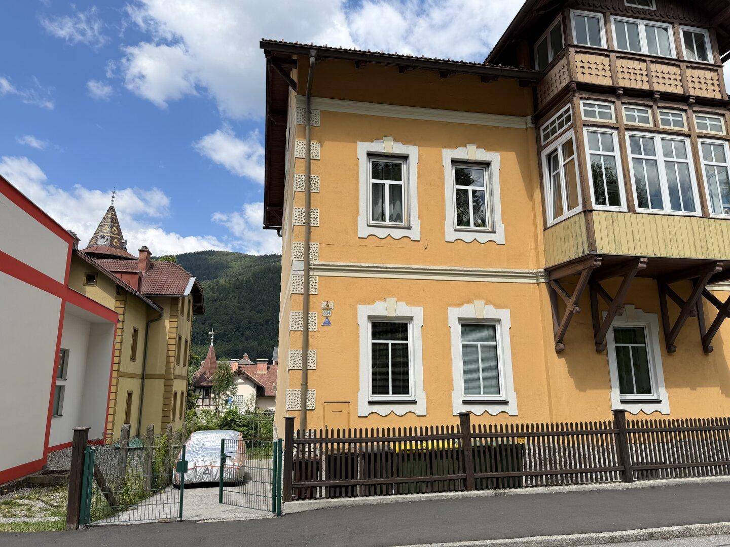 Seitenansicht des historischen Gebäudes mit gelber Fassade, Erker und Blick auf die umliegende Landschaft.