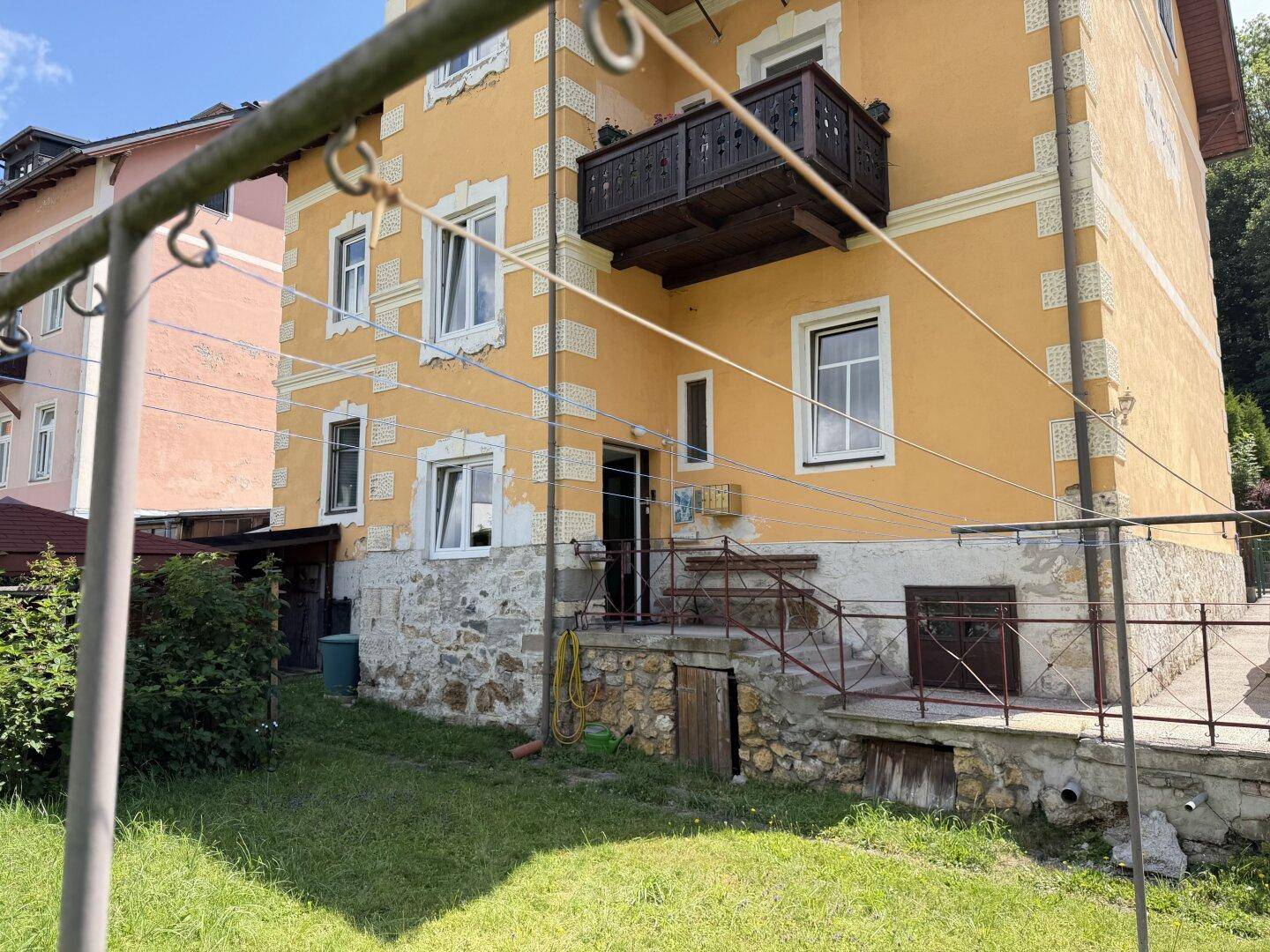 Rückseite des Gebäudes mit kleinem Balkon, Steinfundament und Zugang zum Gartenbereich.