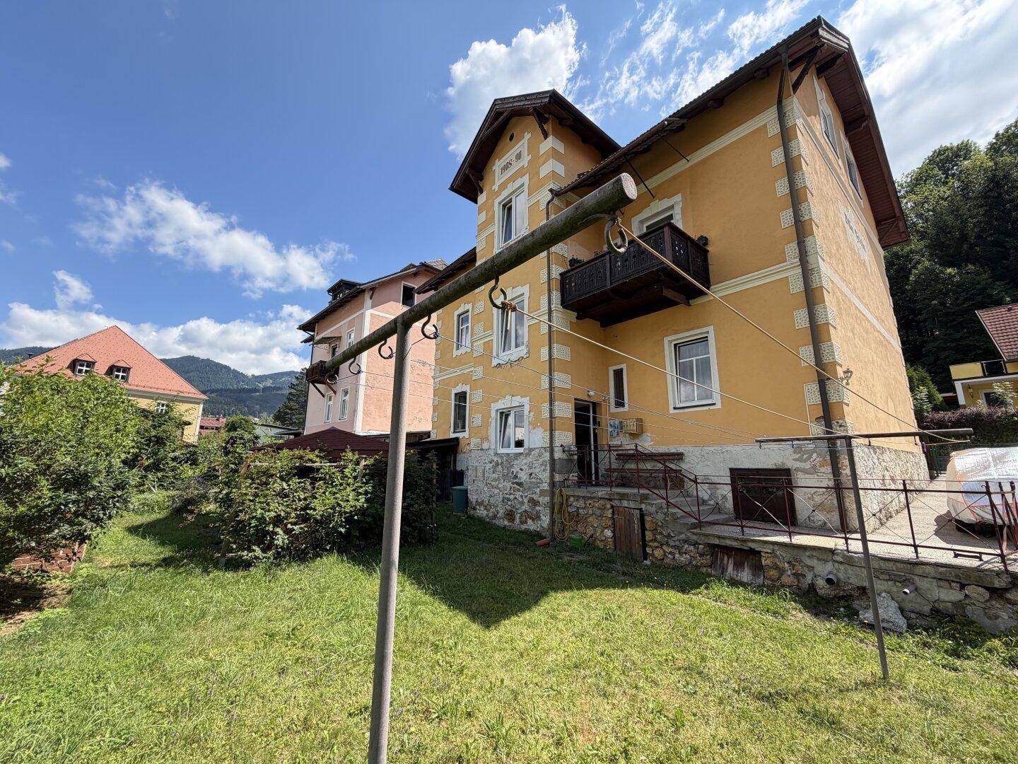Weitläufiger Blick auf die Rückseite des historischen Gebäudes mit Garten und kleinem Balkon.
