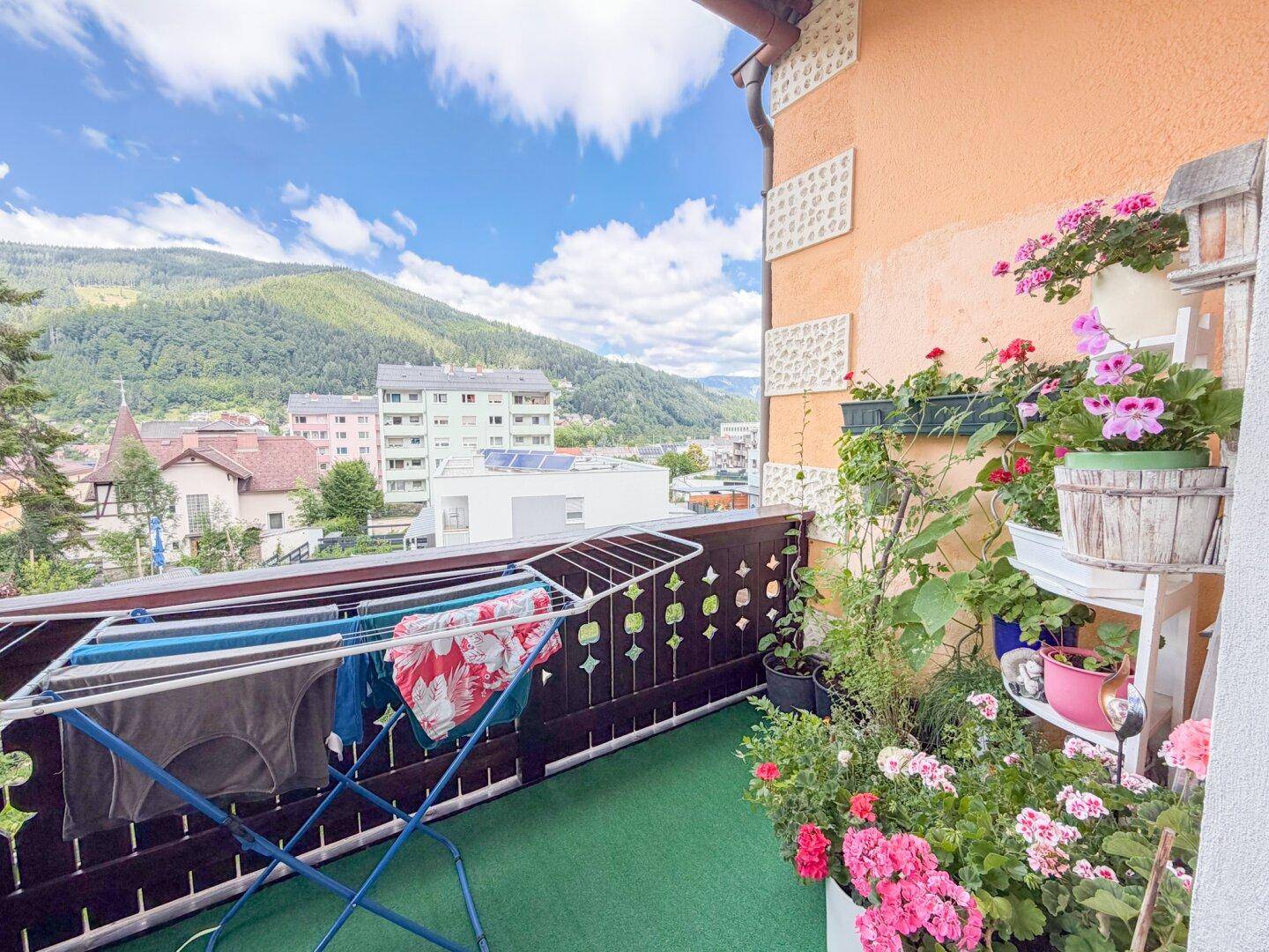Gemütlicher Balkon mit vielen Blumen, Wäscheständer und weitem Blick auf die Berge.