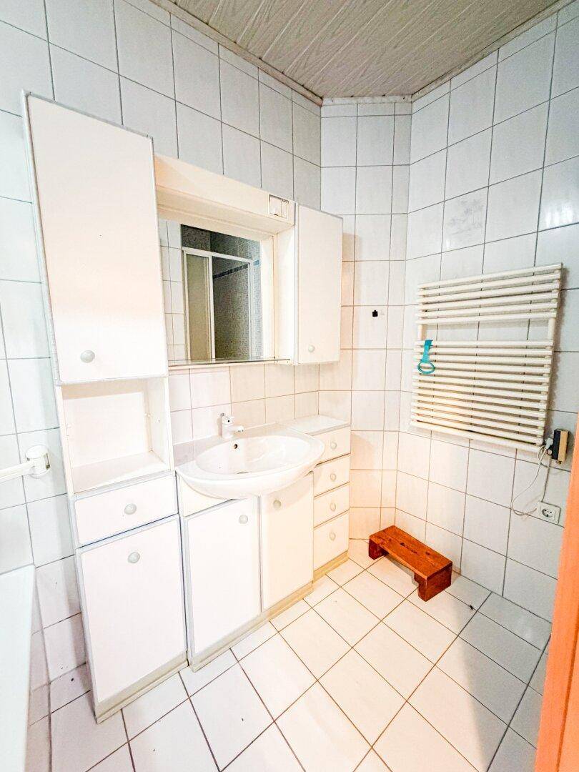 Gefliestes Badezimmer mit Waschbecken, Spiegelschrank und Handtuchheizkörper.