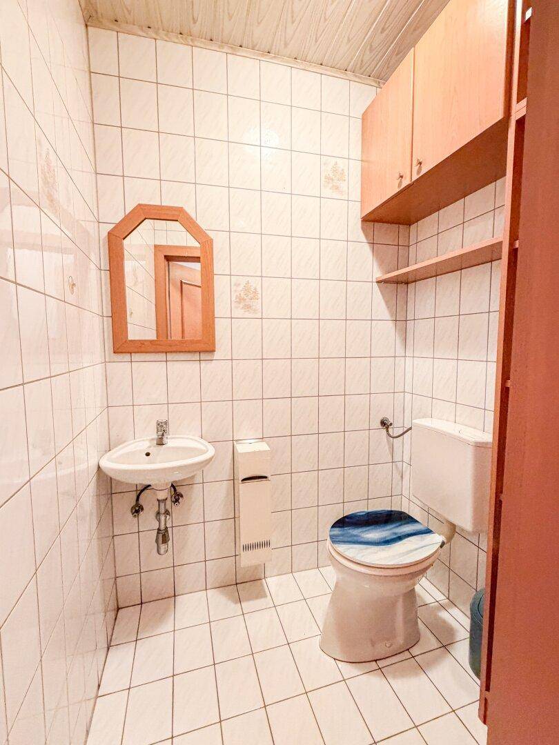 Kleines WC mit Waschbecken, Spiegel und weißen Fliesen.