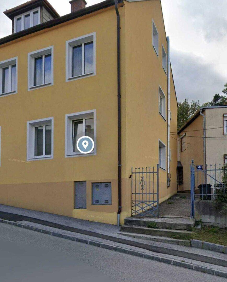 Seitenansicht des gelben Gebäudes mit einem schmiedeeisernen Tor und einem Eingangsbereich an einer ansteigenden Straße.
