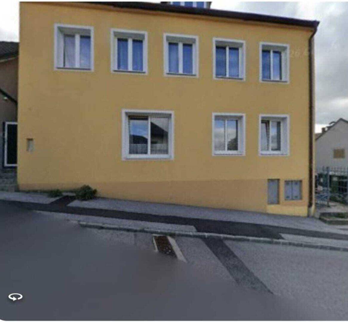 Fassade eines gelben Gebäudes mit vielen weißen Fenstern und einem helleren Sockelbereich an einer Straße.