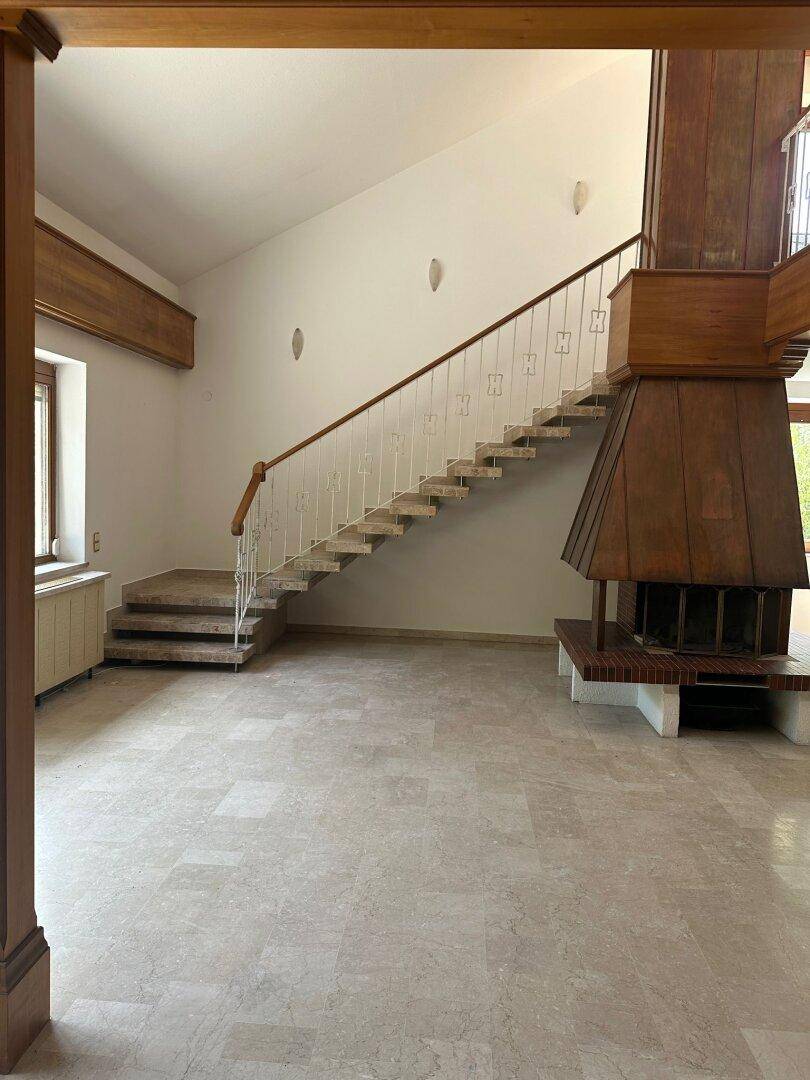 Geräumiger Wohnbereich mit großem Kamin, eleganter Treppe und hellem Marmorboden.
