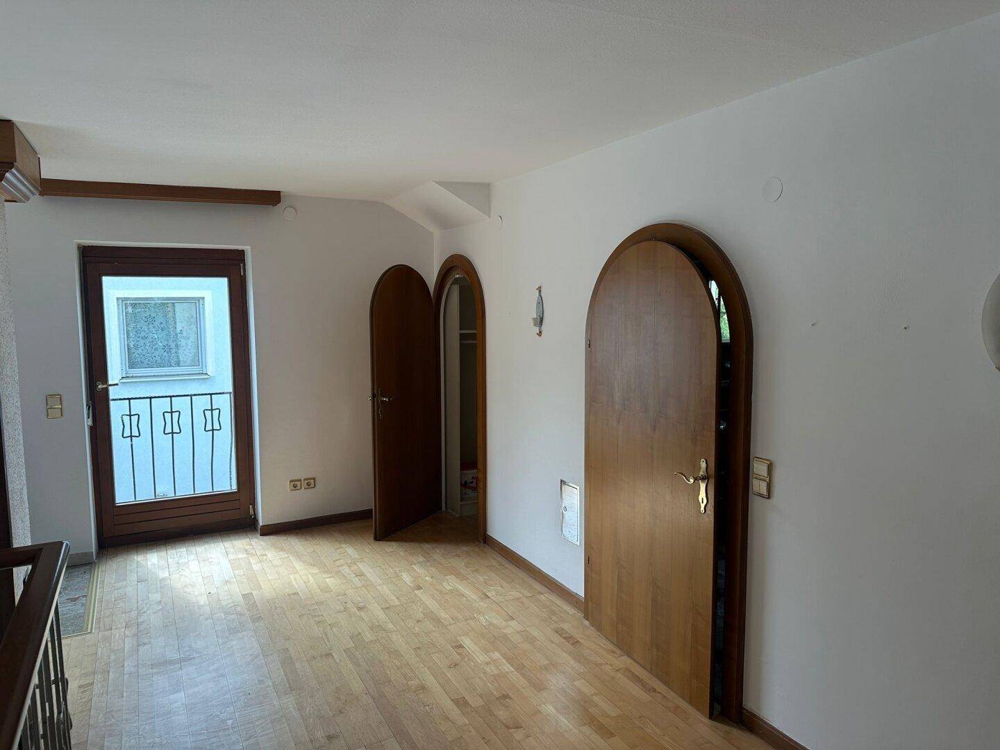 Heller Flur mit Holzboden, Rundbogentüren und einem französischen Balkon.