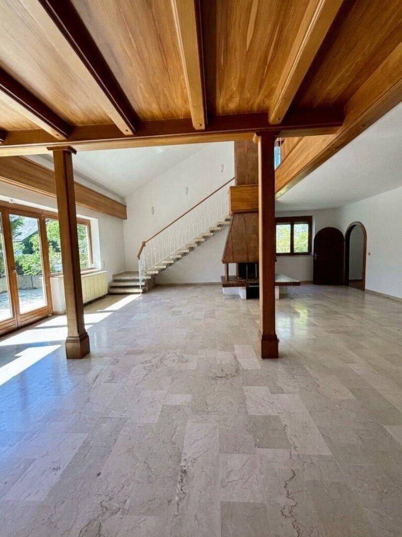 Heller Wohnbereich mit Holzbalken, Kamin und großen Glastüren zum Außenbereich.