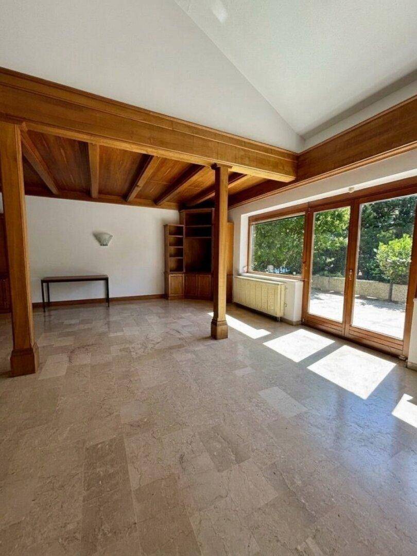Heller Wohnbereich mit Holzbalken und großen Glastüren, die viel Tageslicht hereinlassen.