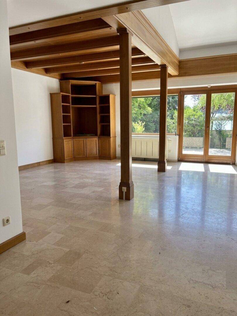 Geräumiges Wohnzimmer mit Holzbalken, Einbauregalen und Zugang zum Außenbereich.