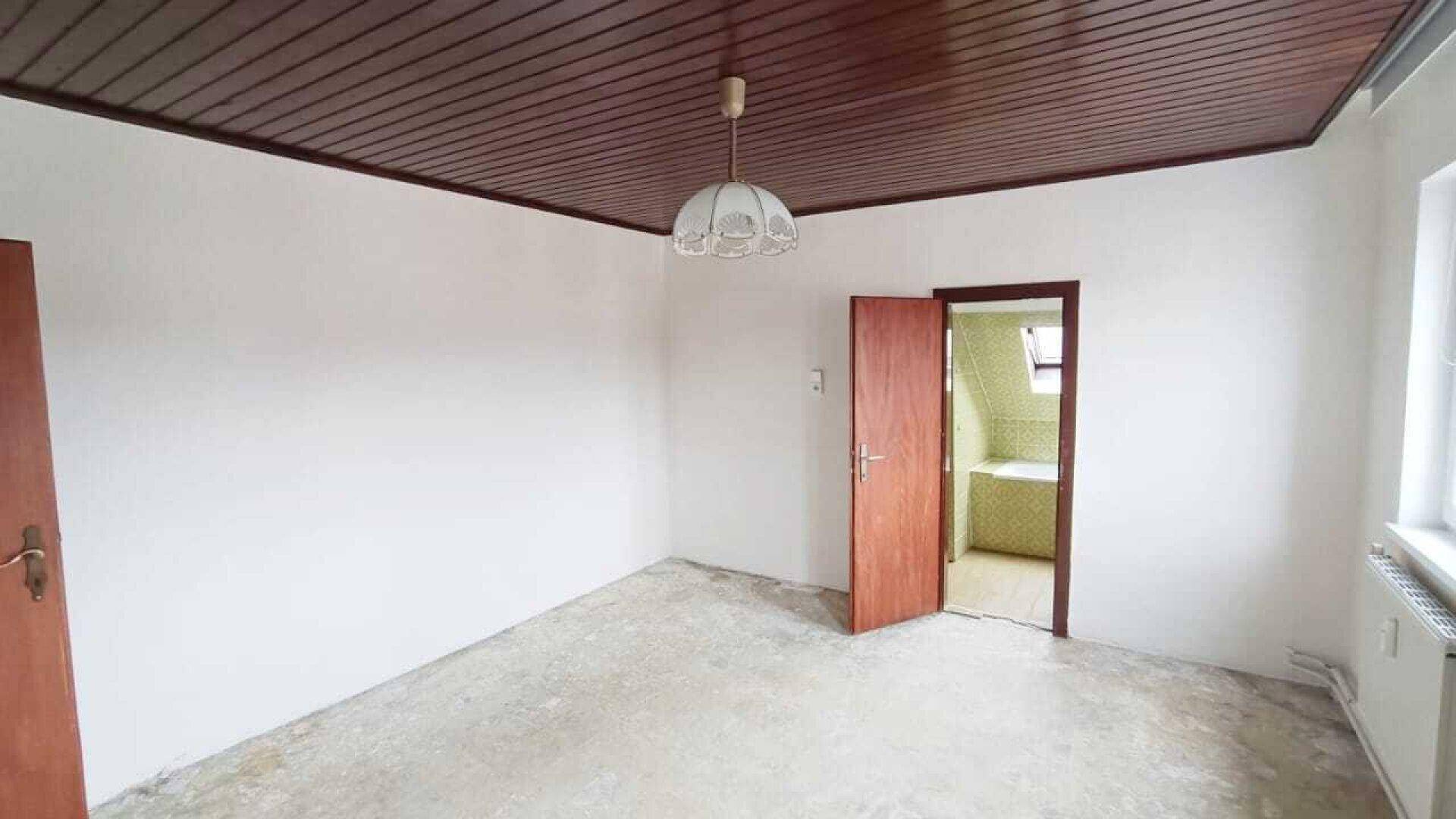 Leerer Raum mit Holztür, Holzdecke und Blick in ein angrenzendes Badezimmer.