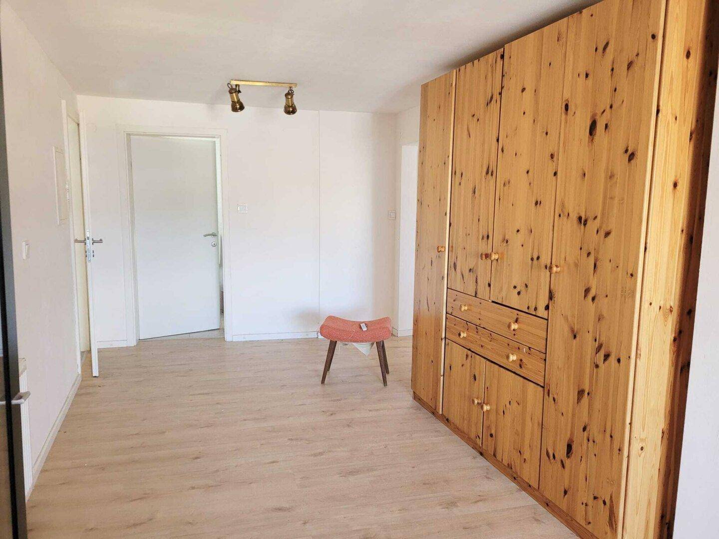 Helles Zimmer mit großem Holzschrank, Laminatboden und weiß gestrichenen Wänden.