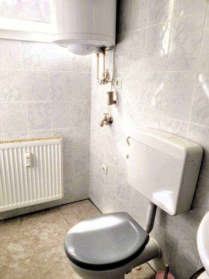 Kleines Badezimmer mit Toilette, Heizkörper und Boiler an der Wand.