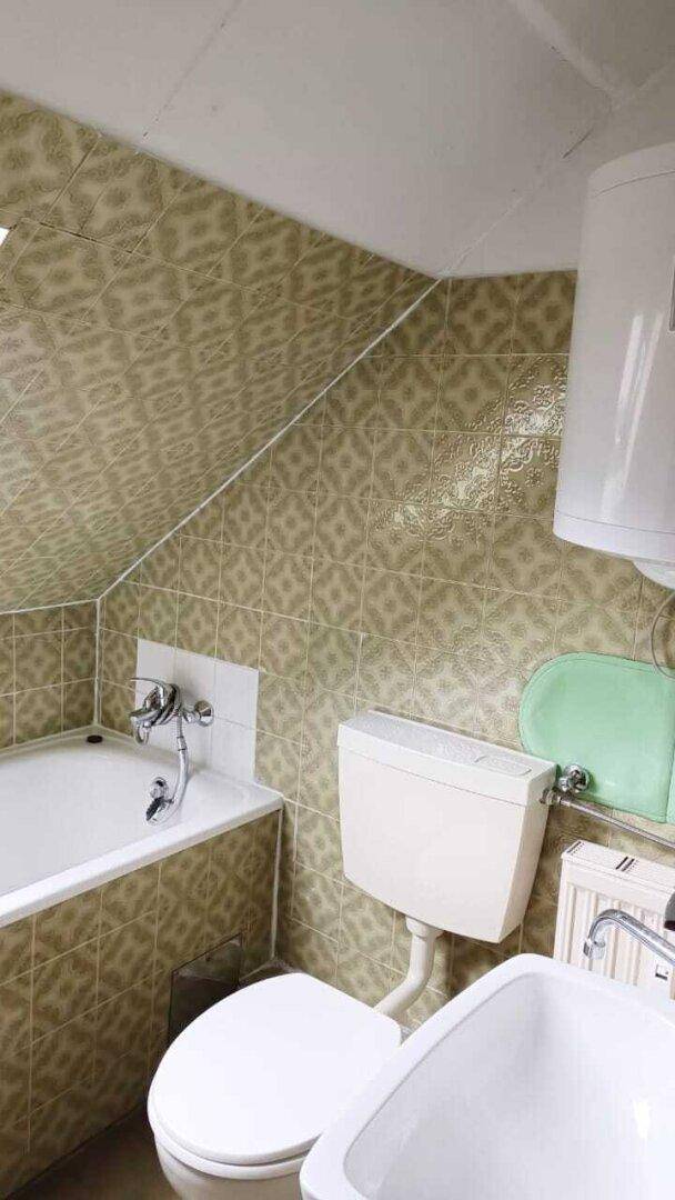 Dachschrägen-Badezimmer mit Badewanne, Toilette und gemusterten grünen Wandfliesen.