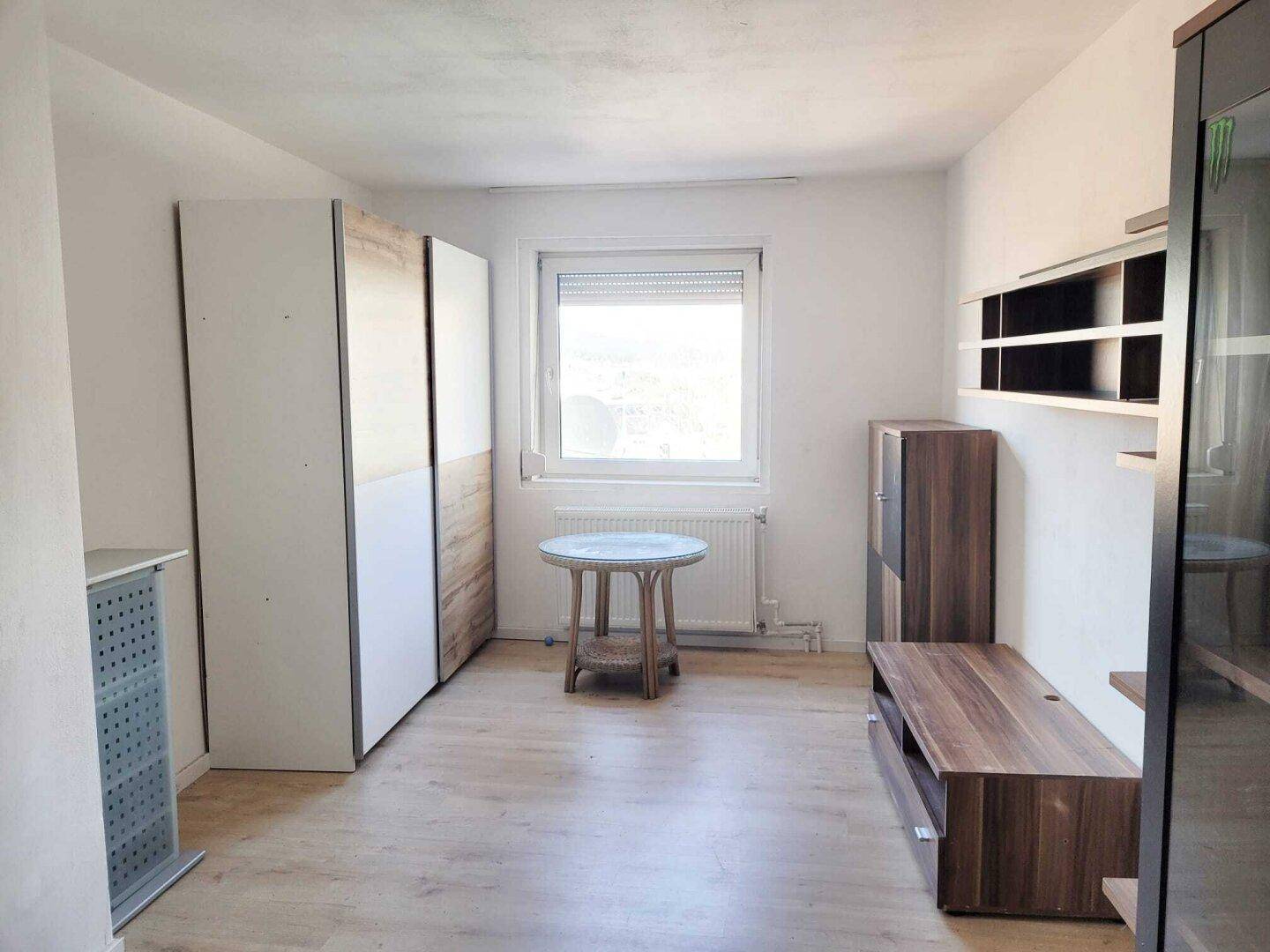 Heller Raum mit Laminatboden, Fenster und modernen Holzmöbeln.