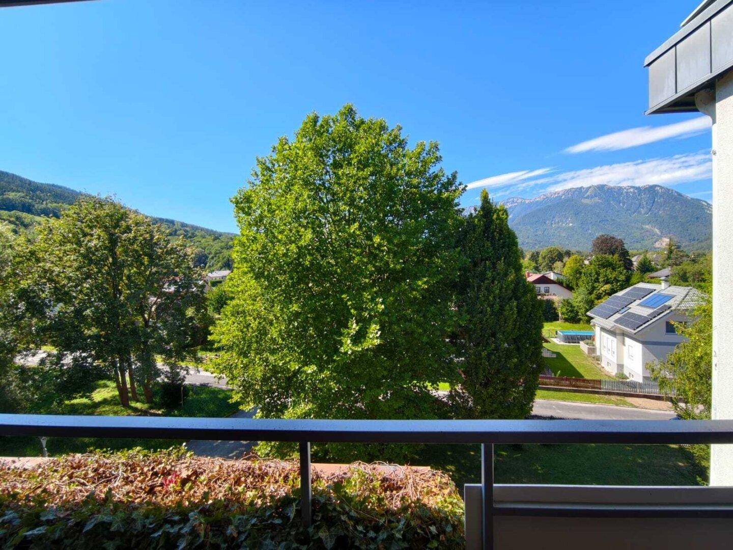 Panoramablick von einem Balkon auf grüne Hügel, ein Haus mit Solaranlage und die umliegende Berglandschaft.