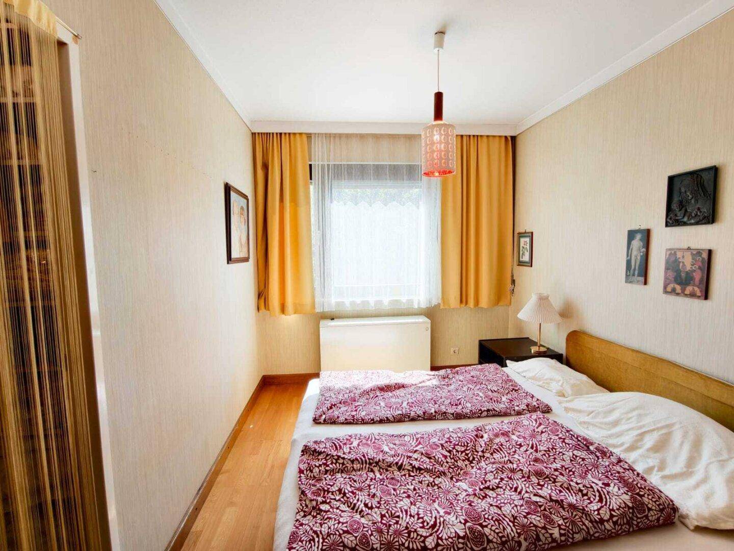 Gemütliches Schlafzimmer mit zwei Einzelbetten, Holzfußboden und gelben Vorhängen, hell durch das Fenster.