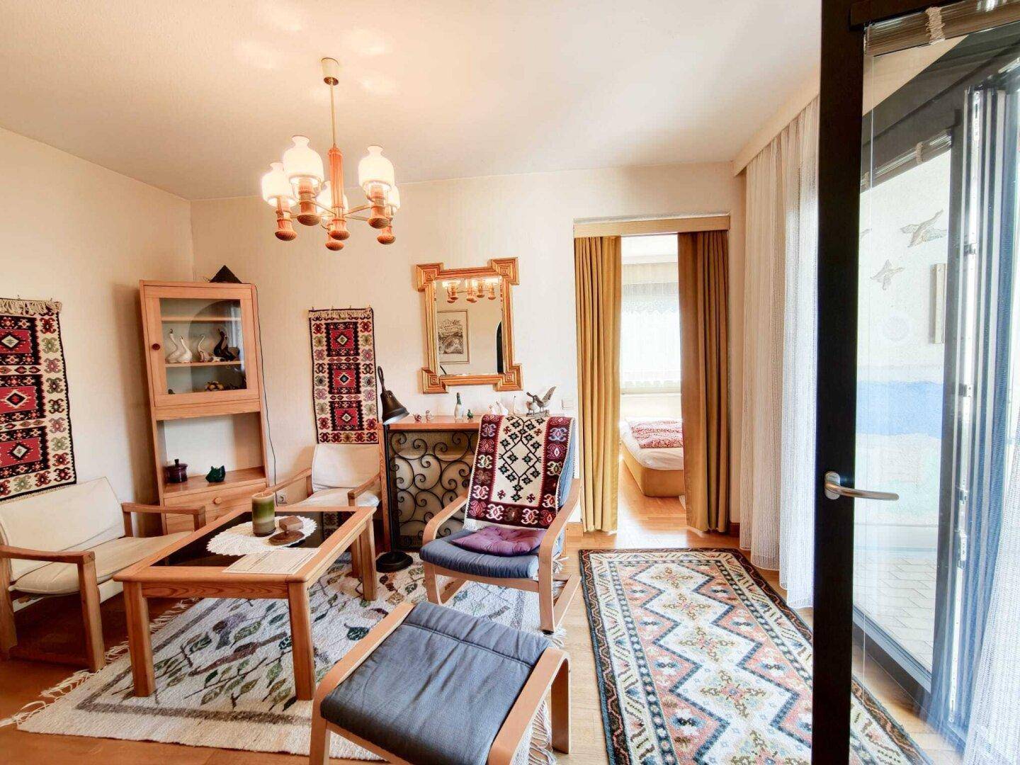Wohnzimmer mit traditionellen Teppichen, Holzmöbeln und Zugang zu einem Balkon, hell und einladend.