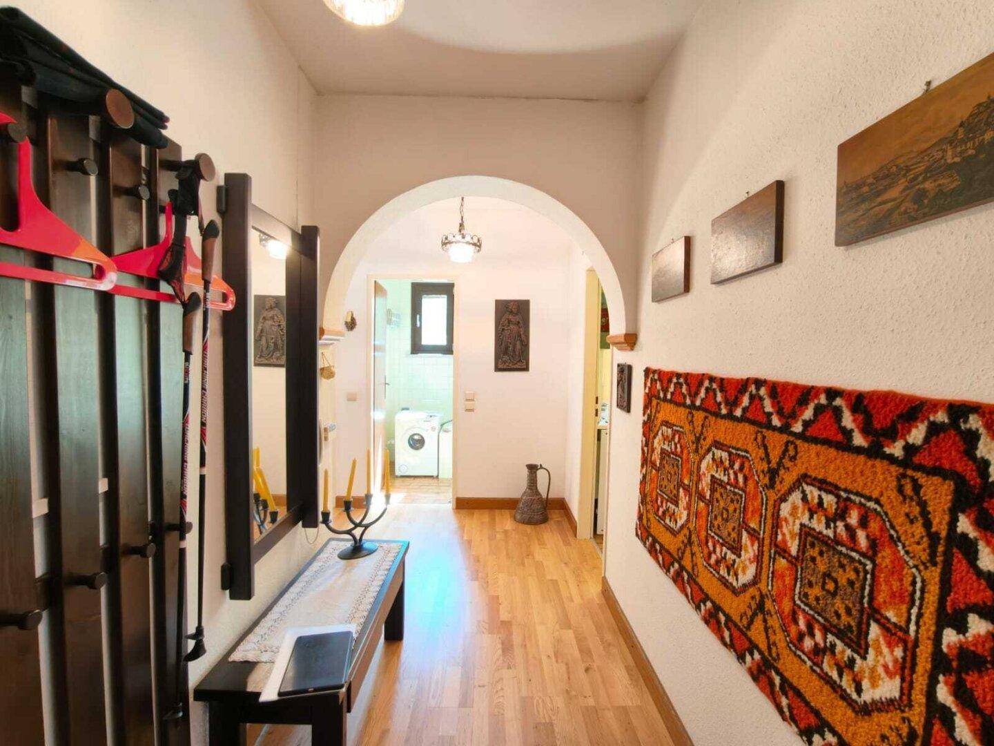 Heller Flur mit Holzboden, einem Bogen und traditionellen Teppichen, der zu weiteren Räumen führt.