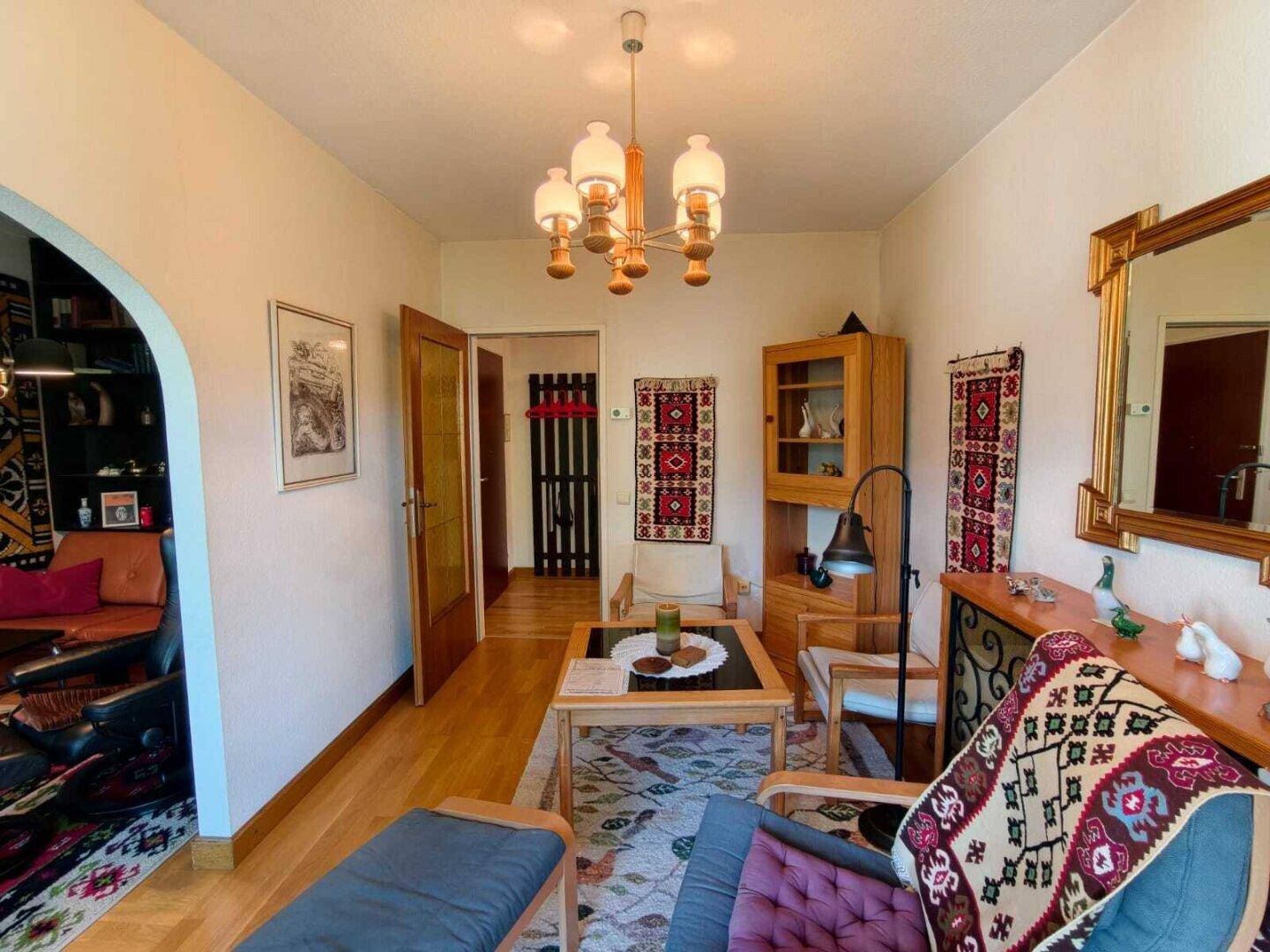 Wohnzimmer mit Holzboden, traditionellen Teppichen und einem Bogen, der zu einem weiteren Bereich führt.