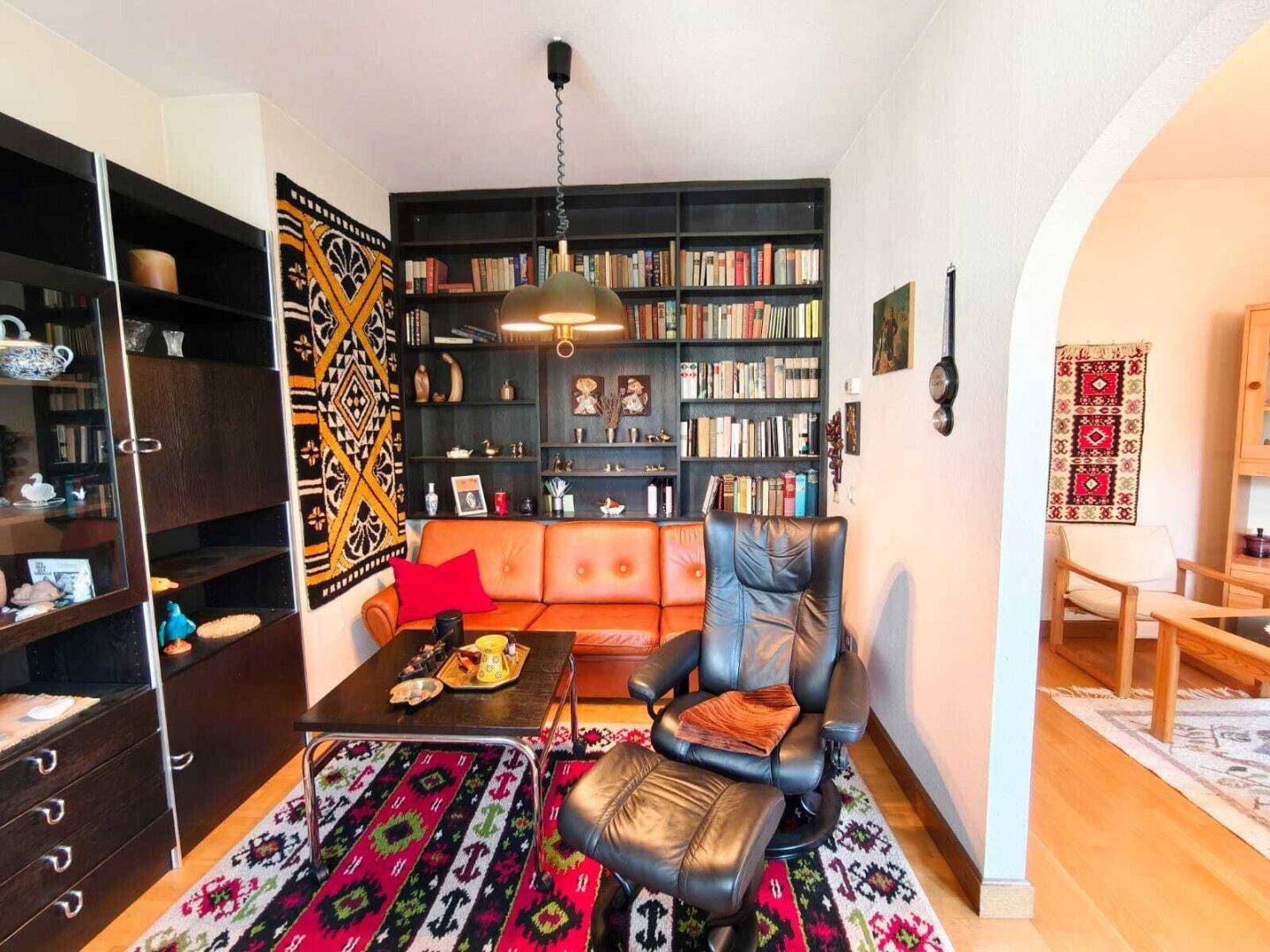 Gemütliches Wohnzimmer mit Ledersofa, großem Bücherregal und farbenfrohen Teppichen, ideal zum Entspannen.