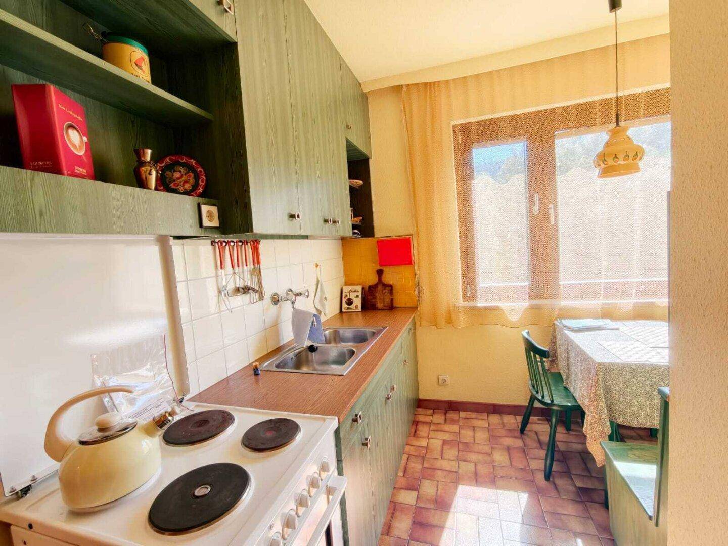 Funktionale Küche mit grünen Schränken, einem Herd und einem Essbereich am Fenster, hell und praktisch.