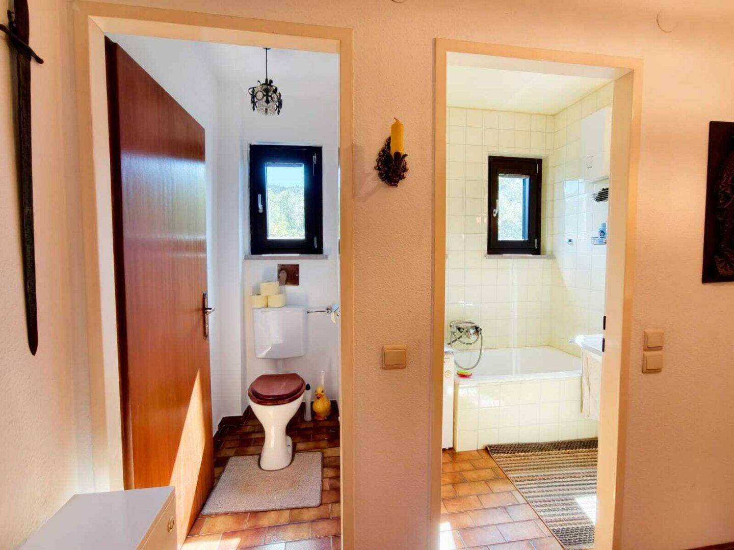 Zwei Türen führen zu einem separaten WC und einem Badezimmer mit Badewanne, beide mit Fenstern.
