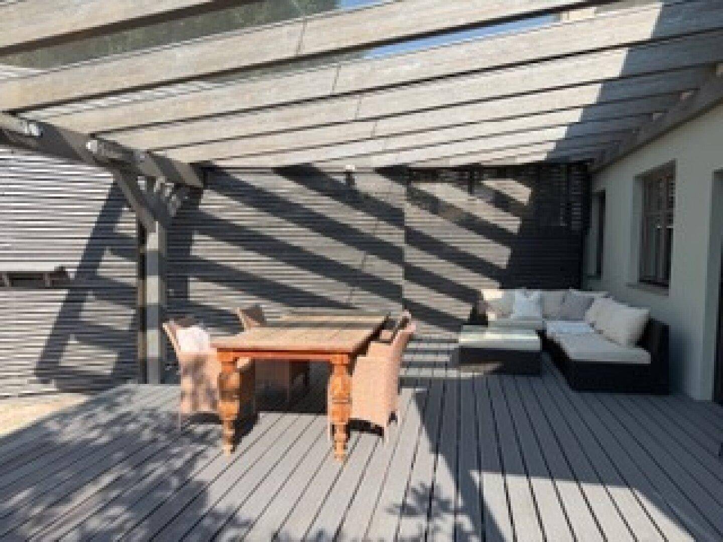 Überdachte Holzterrasse mit Essbereich und gemütlicher Lounge-Ecke im Freien.