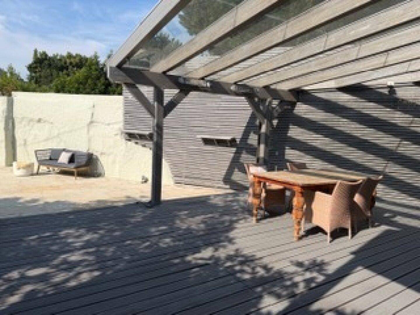 Weitläufige Holzterrasse mit Essbereich und Lounge-Möbeln unter einer Pergola.