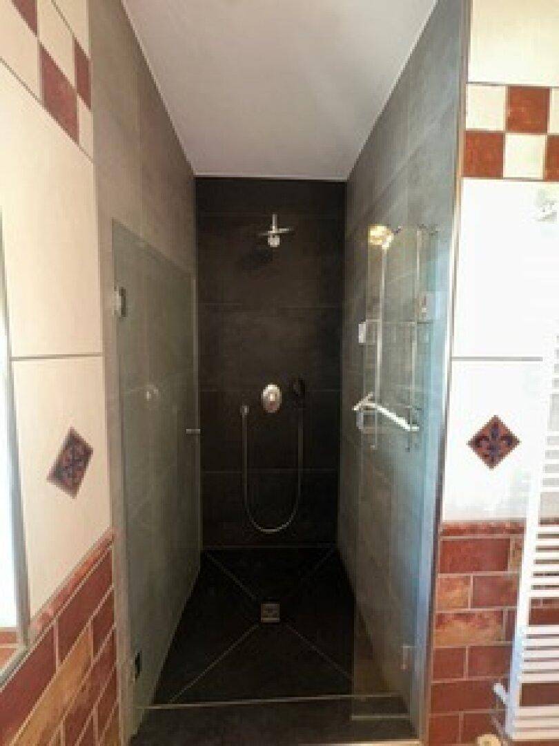 Moderne Duschkabine mit dunklen Fliesen und Glasabtrennung im Badezimmer.